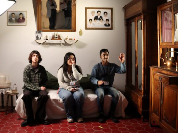 Three young people sit within a scene created by Zineb Sedira