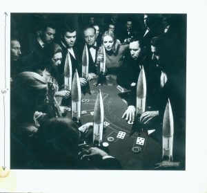 Peter Kennard's photomontage of people standing around a poker table, all the chips are nuclear bombs
