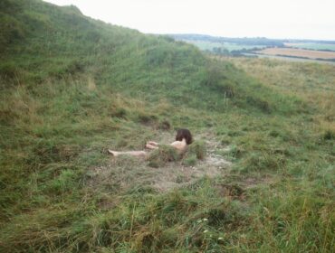 A photo of a naked person lying in a field of green grass