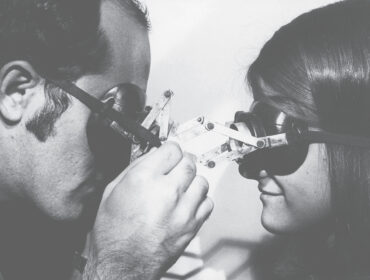 black and white image of two people looking at each other through goggles