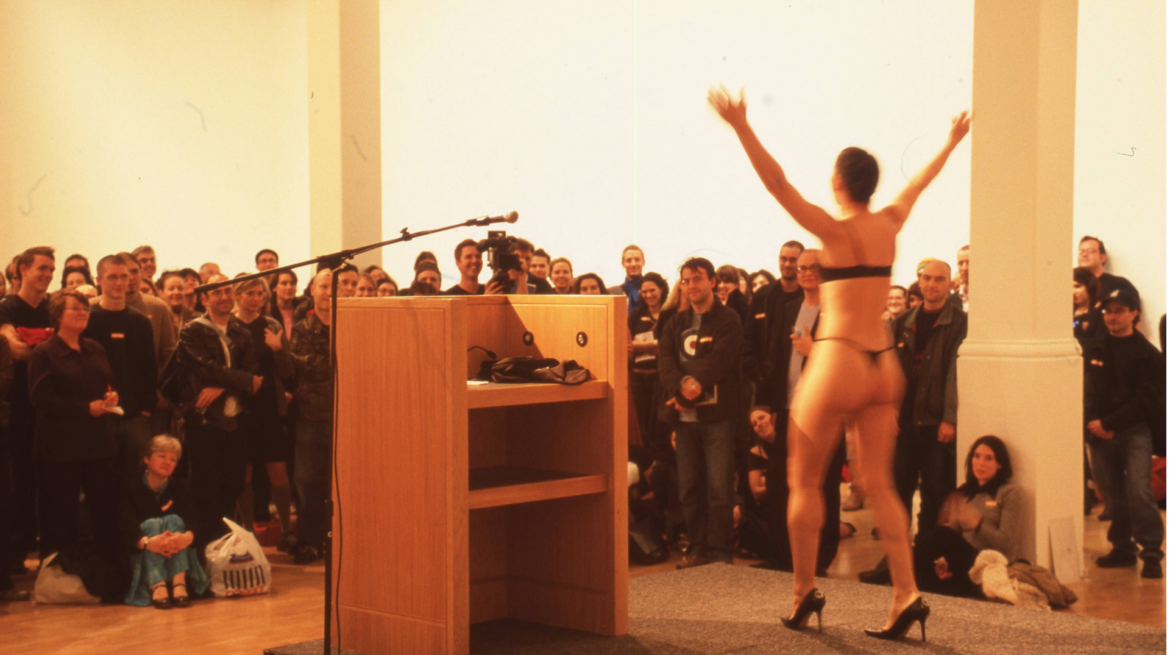 Woman in underwear performing at podium to audience