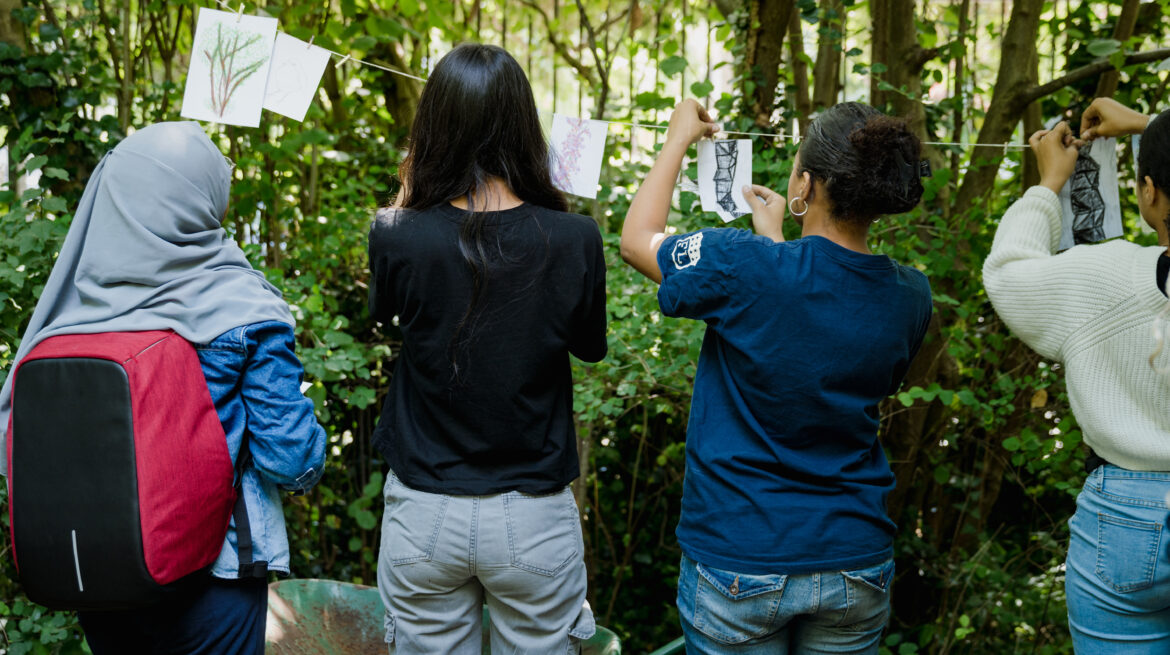 Young people hang drawings on string between trees in nature reserve