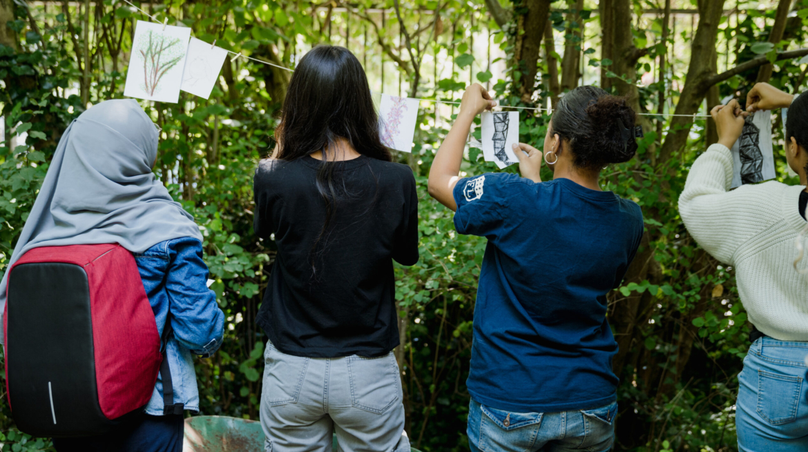 Young people hang drawings on string between trees in nature reserve